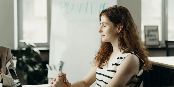 Empresária sentada à mesa do escritório diante do notebook, com quadro de planejamento ao fundo, avaliando se pode ter mais de uma empresa no mesmo CPF