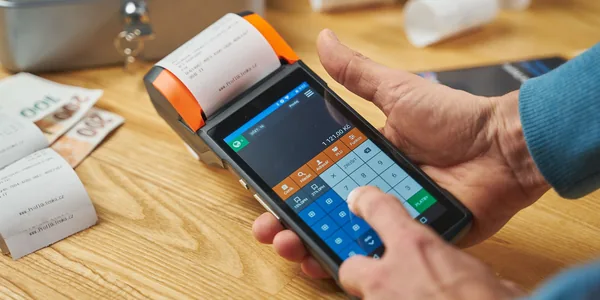 Mãos operando uma maquininha de cartão que imprime o comprovante