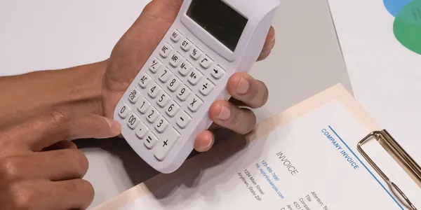Mãos usando calculadora ao lado de uma nota fiscal para calcular o IBS e a CBS