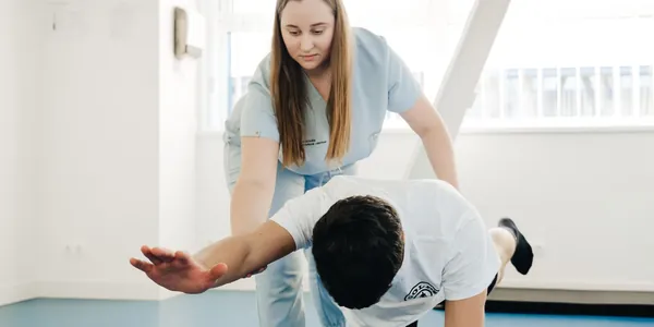Fisioterapeuta de uniforme azul alongando o braço de um paciente na clínica