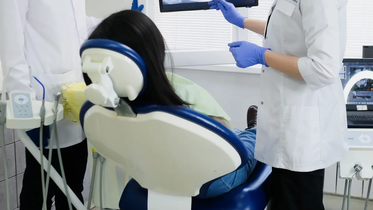 Dois profissionais de odontologia observando uma radiografia na tela ao lado da cadeira