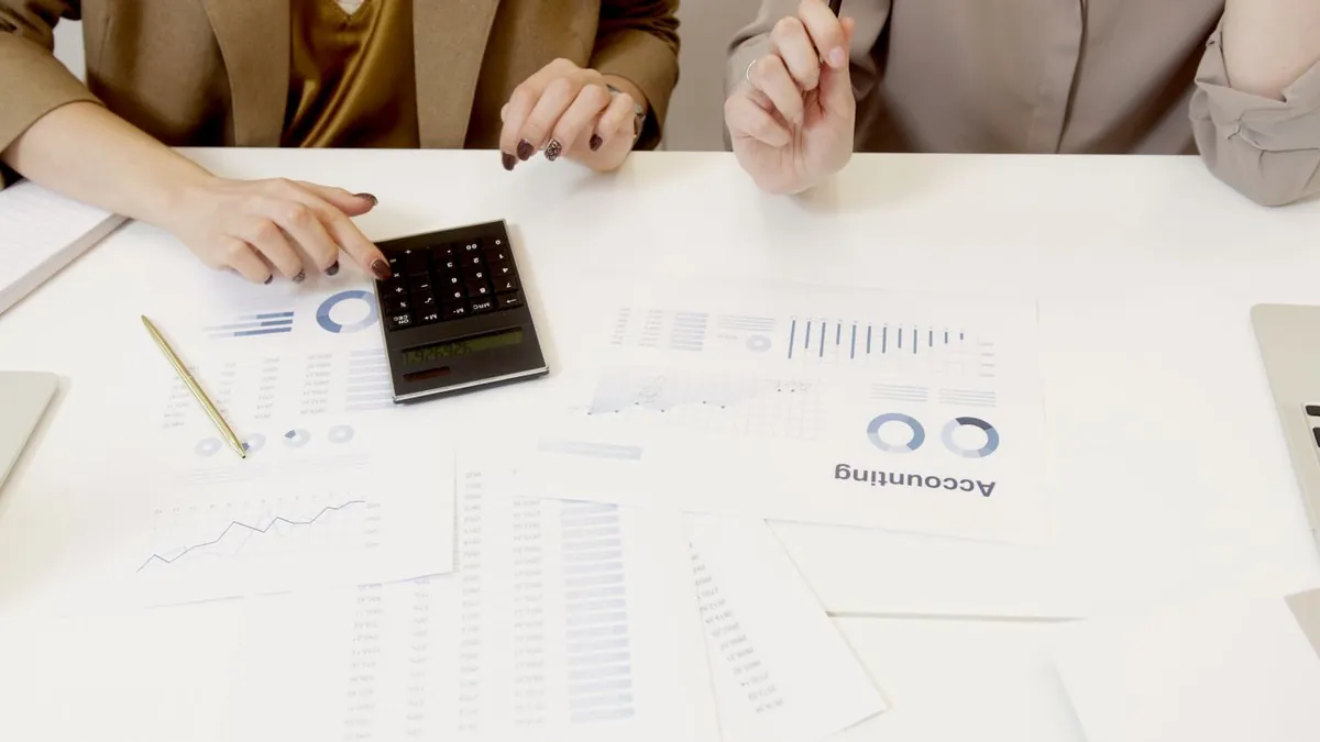 Três pessoas em volta da mesa com calculadora, gráficos e relatórios impressos