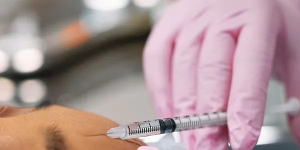 Profissional de luvas rosa aplicando um injetável na testa de um cliente