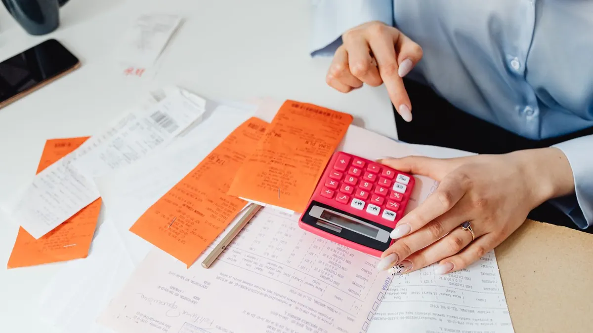 Mãos conferindo recibos com uma calculadora rosa sobre a mesa