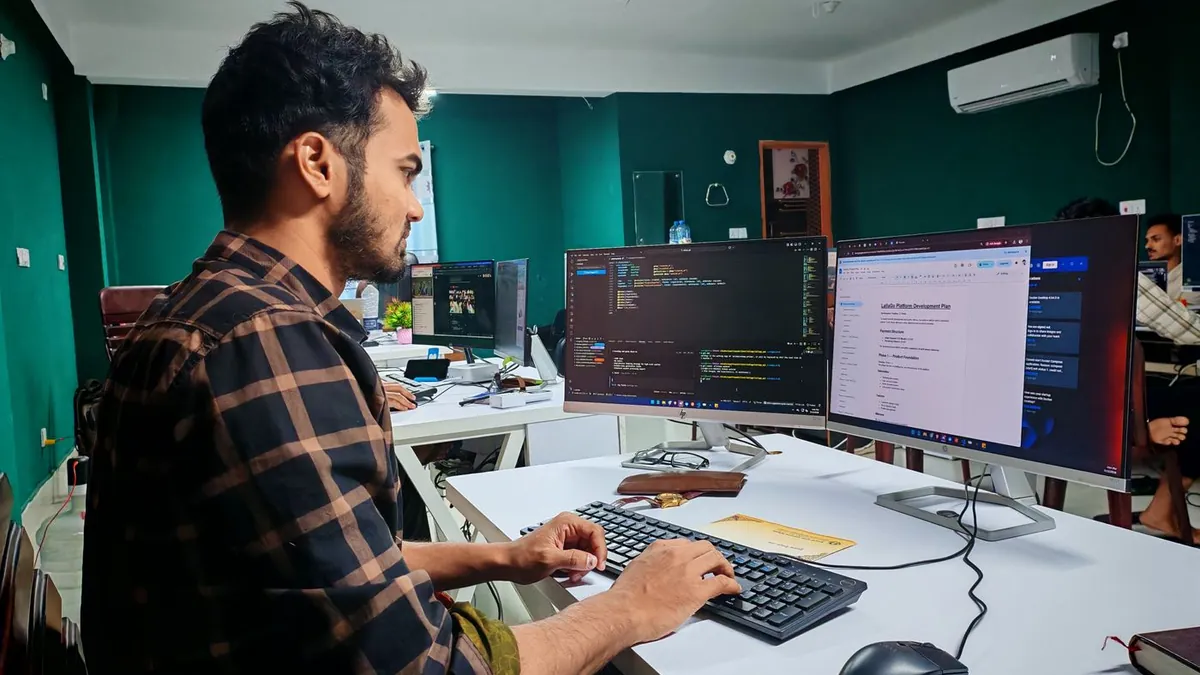 Desenvolvedor de camisa xadrez trabalhando em dois monitores no escritório