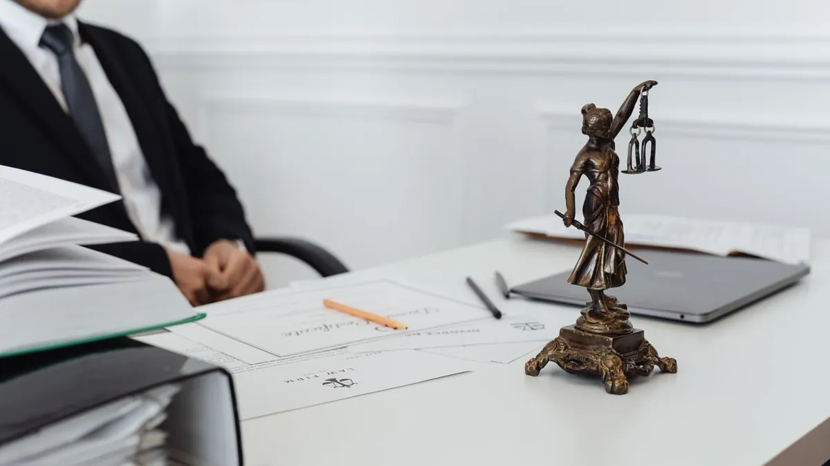 Estátua da Justiça sobre a mesa do escritório, com documentos e um notebook ao fundo