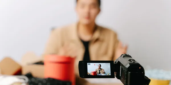 Câmera sobre tripé gravando uma pessoa sentada à mesa, desfocada ao fundo
