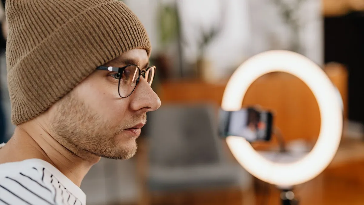 Homem de gorro e óculos gravando com o celular preso ao ring light