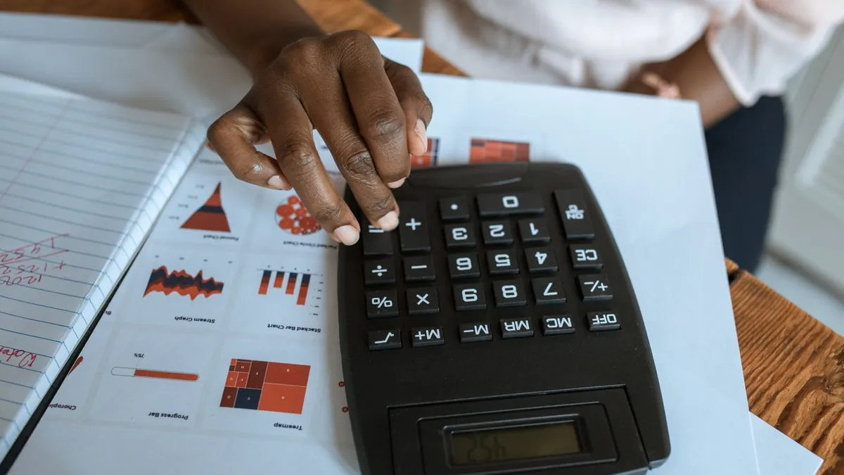 Mão usando calculadora sobre planilhas e gráficos impressos