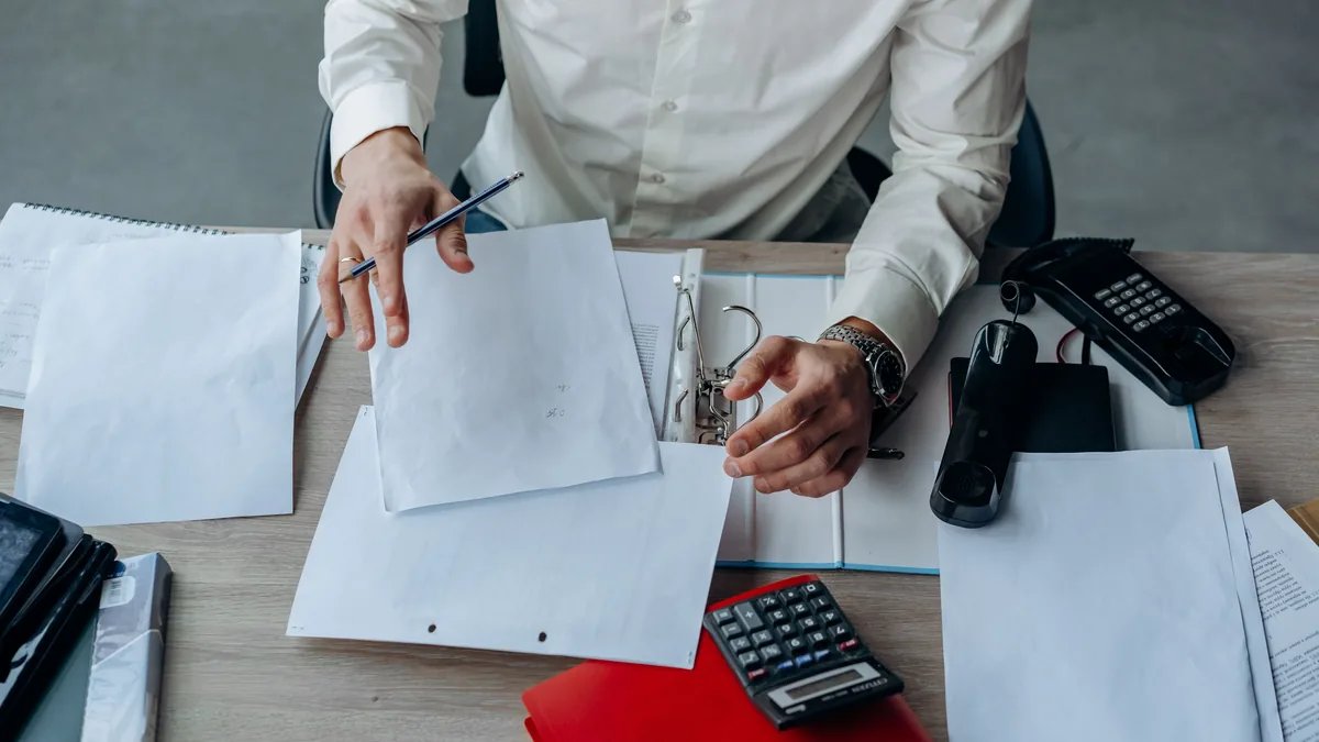 A business professional organizing documents at a busy office desk, emphasizing productivity.
