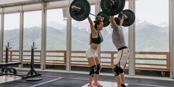 A couple lifting barbells together in a gym with scenic mountain views.