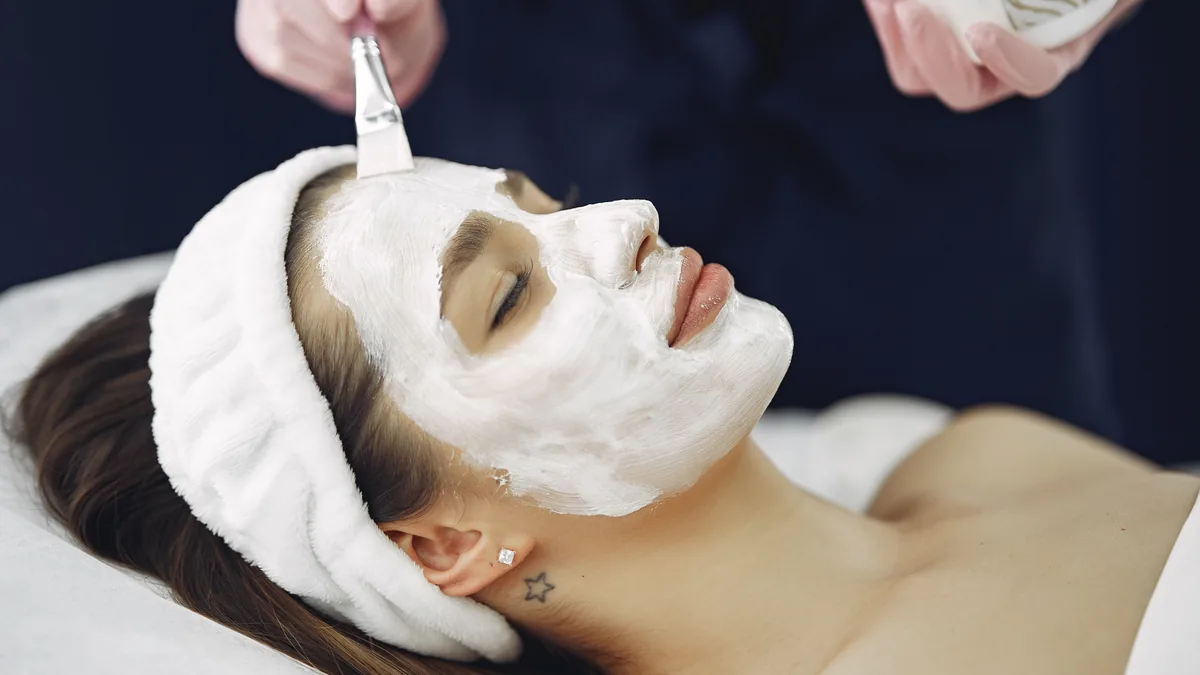 Close-up of a woman with eyes closed enjoying a calming facial mask application at a spa.