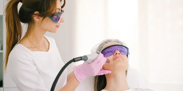A cosmetologist performing laser treatment on a woman in a clinic setting.