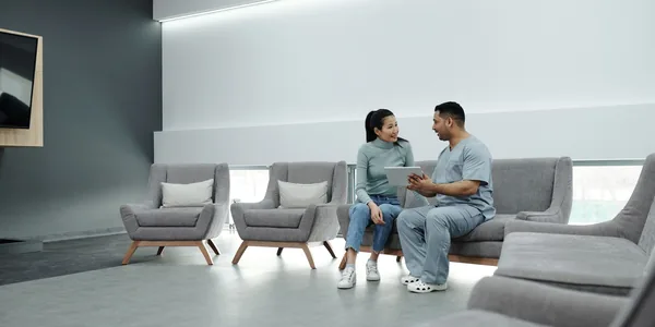 Doctor and patient discussing health in a modern waiting room with digital tablet.