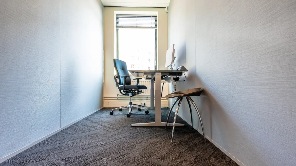 A clean, minimalist office space featuring a desk, chair, and computer by a large window.