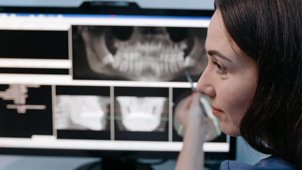 Female dentist reviewing digital dental x-rays on a computer screen in a clinic setting.