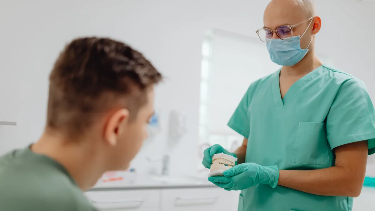 Dentist in scrubs explains dental procedure to a patient in an office setting.