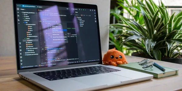 Laptop with coding interface, plant, and toy for a cozy workspace vibe.