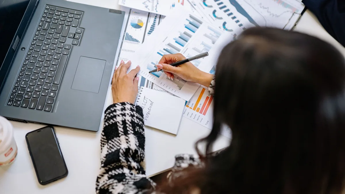 A professional woman reviewing financial charts and graphs with a laptop and smartphone on the desk.