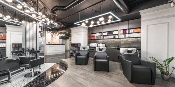 Comfortable backwash chairs with sinks near potted plant placed in contemporary beauty salon with bright illumination and abundance of cosmetology products
