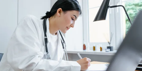 Profissional da saúde de jaleco branco à mesa de um consultório, analisando documentos: imagem ilustrativa de como o médico paga menos imposto sendo PJ