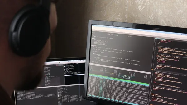 Desenvolvedor escrevendo código em frente a dois monitores