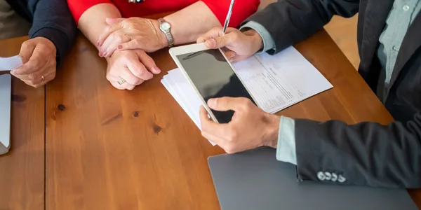 Reunião em mesa de madeira com consultor revisando documentos e usando um tablet