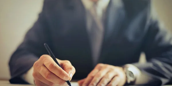Homem de terno assinando um contrato com caneta sobre a mesa de um escritório