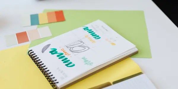 Caderno com propostas de logotipo e cartela de cores sobre a mesa, representando razão social, nome fantasia e marca
