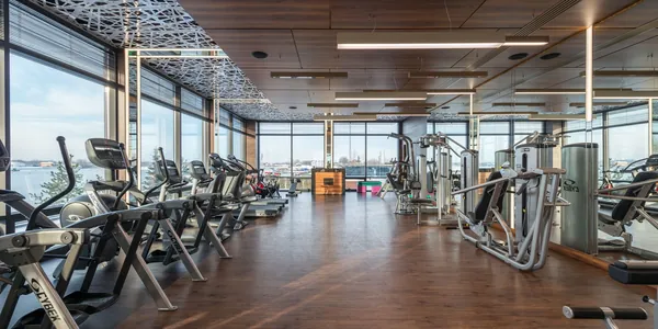 Interior de academia com esteiras e aparelhos de muscula&ccedil;&atilde;o diante de janelas amplas