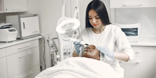 Profissional de est&eacute;tica realizando um procedimento facial em cl&iacute;nica com equipamentos