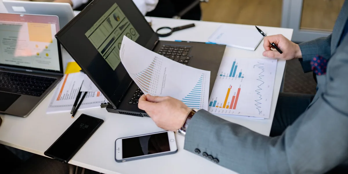 Mesa de reunião com notebook aberto, relatórios impressos e gráficos coloridos