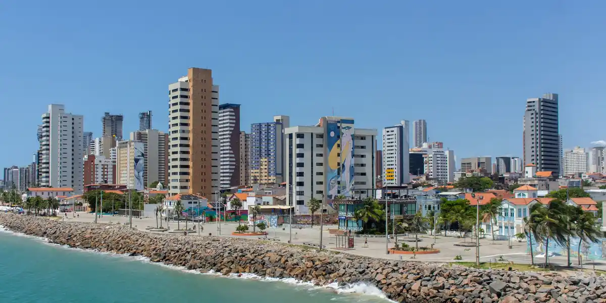 Orla de uma cidade litorânea brasileira, com prédios altos e um espigão de pedras no mar