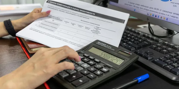 Mãos usando uma calculadora sobre uma planilha na mesa do escritório