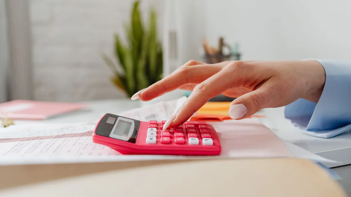 Mão apertando as teclas de uma calculadora sobre papelada de escritório