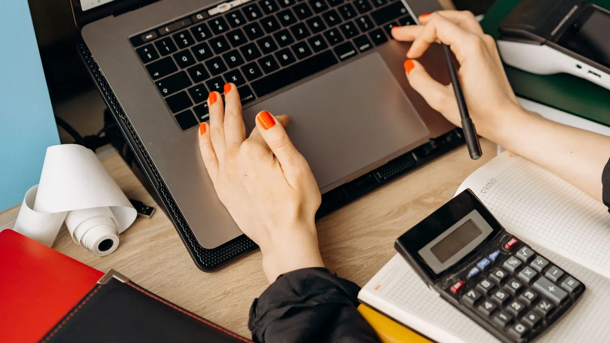 Mulher trabalhando com notebook e calculadora sobre a mesa de madeira