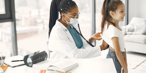 Médica de jaleco branco atendendo uma criança no consultório da clínica
