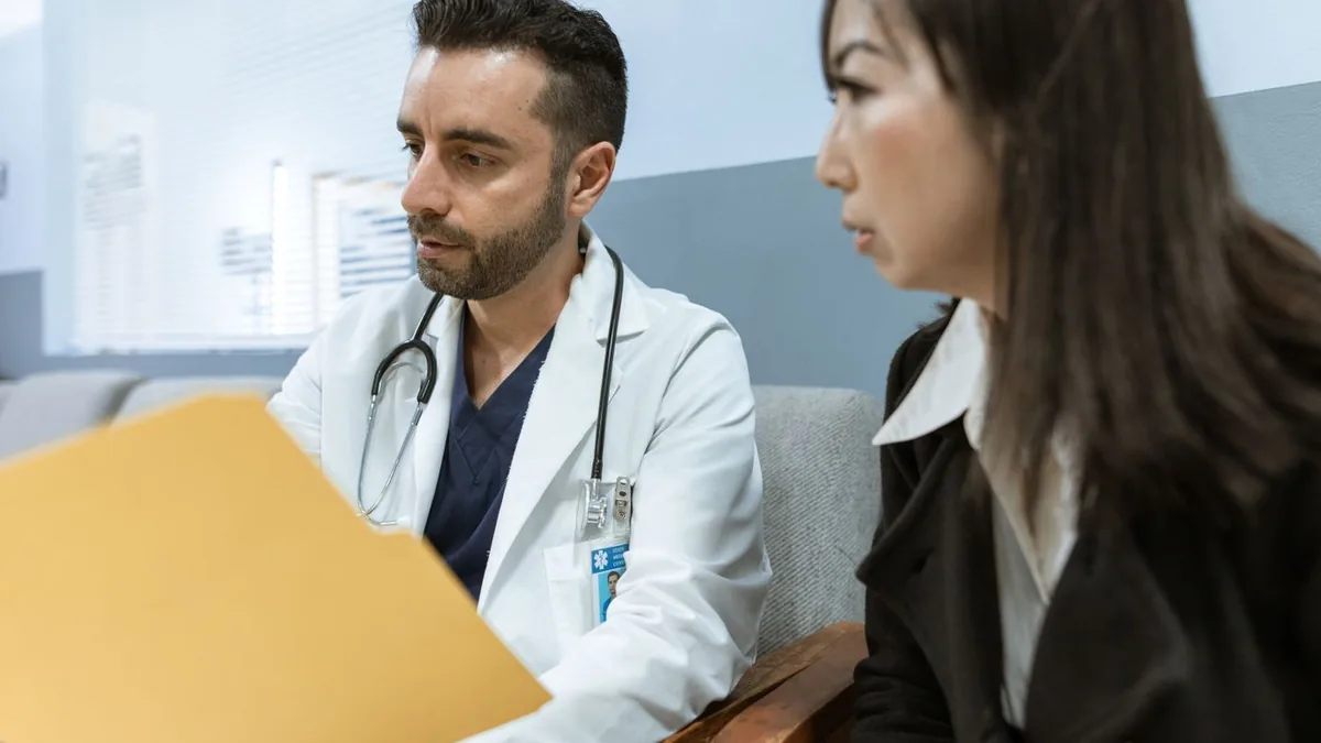 Médico com uma pasta de documentos conversando com uma paciente no consultório