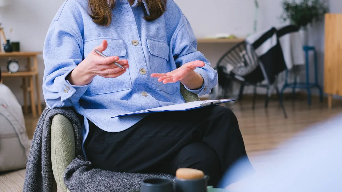 Psic&oacute;loga com uma prancheta no colo conversando durante a consulta