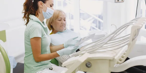 Dentista conversando com uma paciente sentada na cadeira do consultório