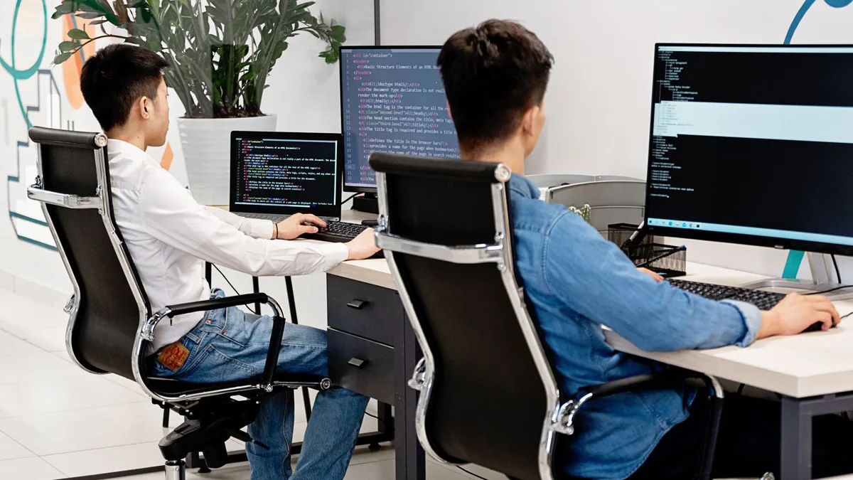 Dois programadores revisando código em monitores num escritório claro