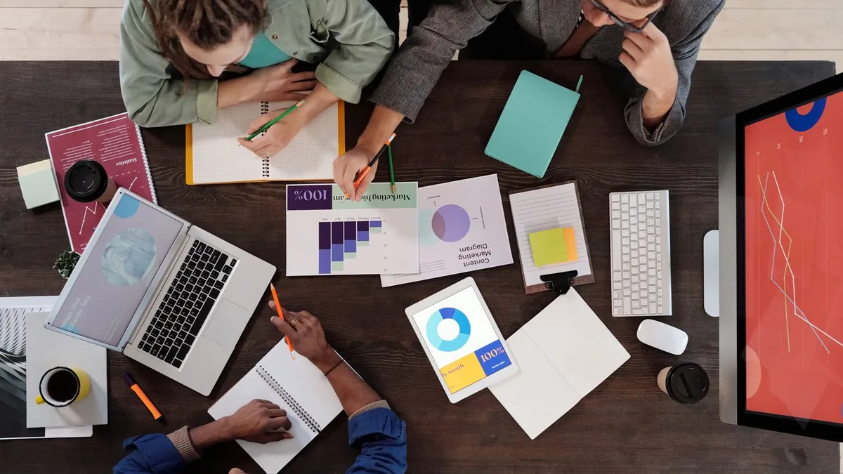 Mesa de trabalho vista de cima com notebooks, gráficos impressos e anotações