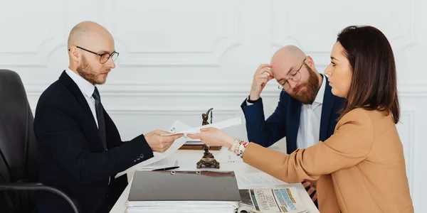 Advogado atendendo dois clientes e revisando documentos no escritório