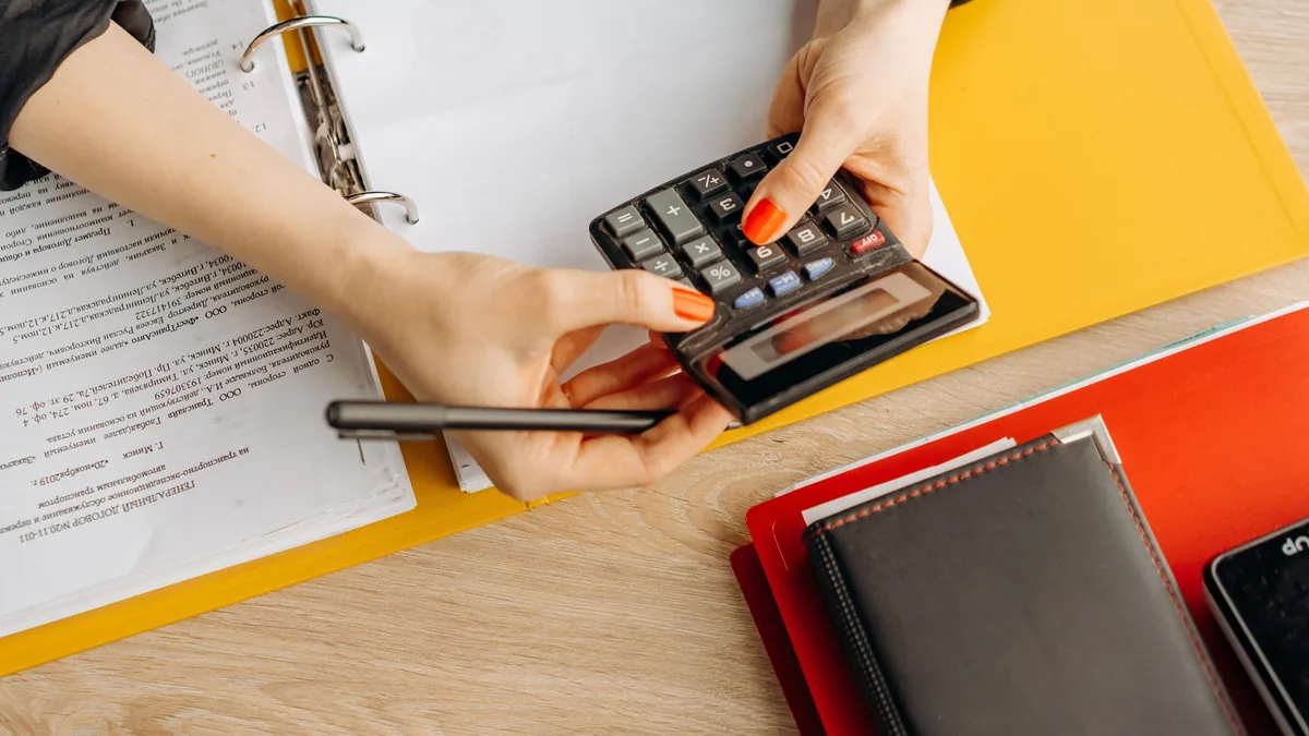Mãos usando calculadora sobre uma mesa com documentos e pastas