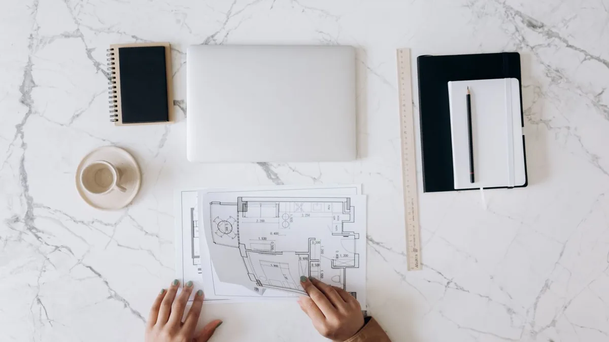 Mesa de arquiteto com planta impressa, régua, caderno e notebook