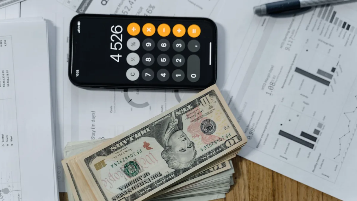 Celular com a calculadora aberta, dinheiro e documentos sobre a mesa