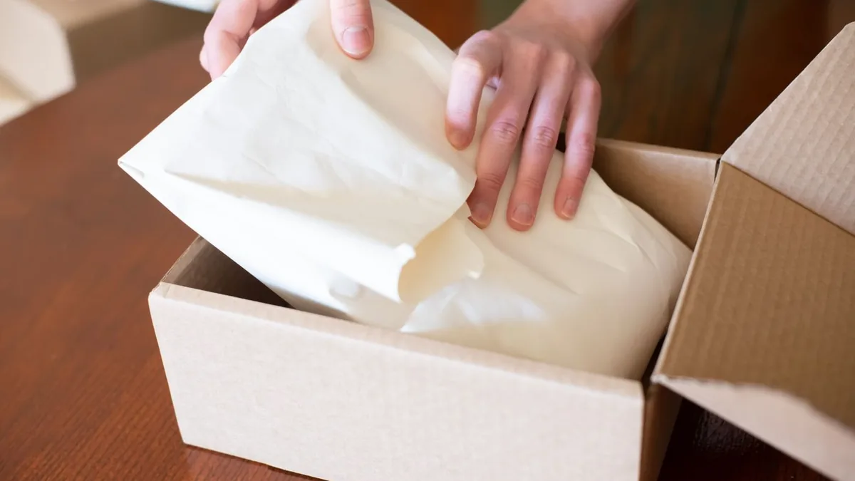 M&atilde;os embalando um pedido dentro de uma caixa de papel&atilde;o