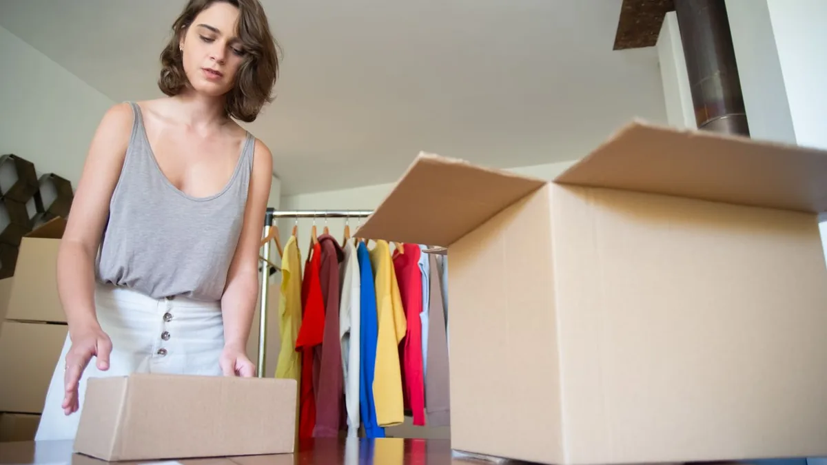 Mulher separando caixas de pedidos ao lado de uma arara de roupas