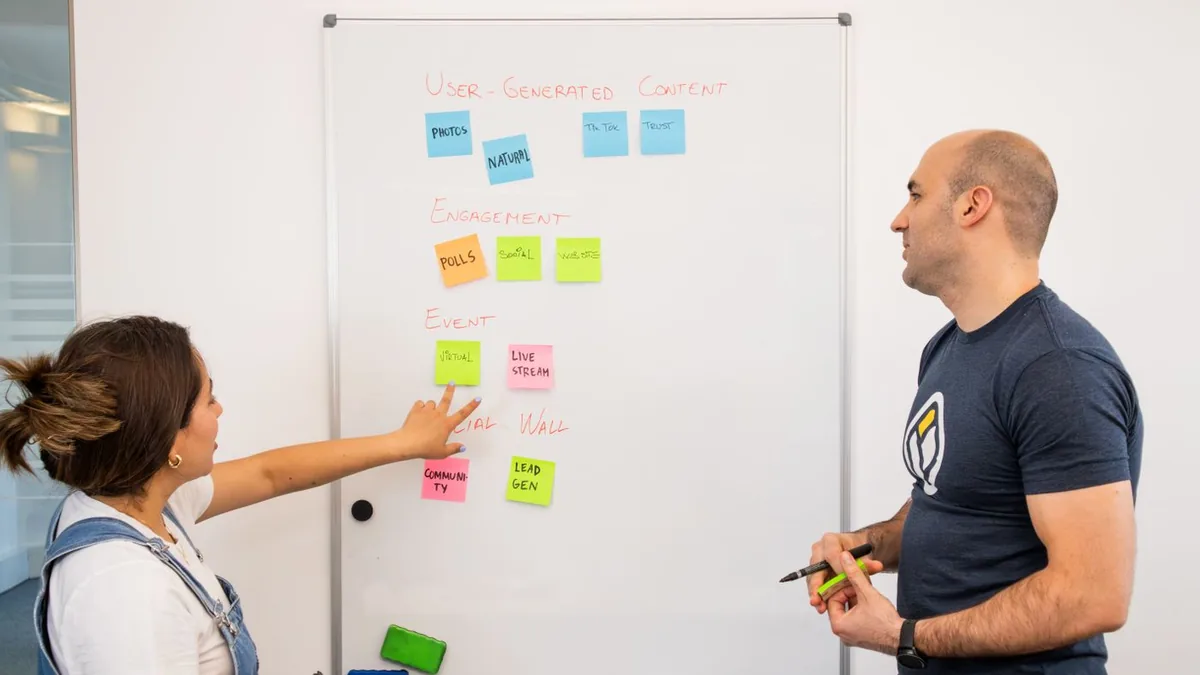 Quadro branco com post-its de planejamento de conte&uacute;do e duas pessoas discutindo