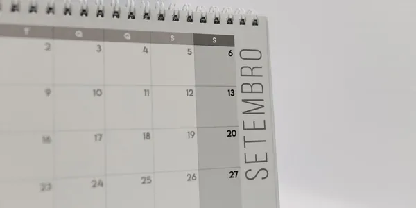 Calendário de mesa com espiral aberto na página de setembro, sobre uma superfície clara